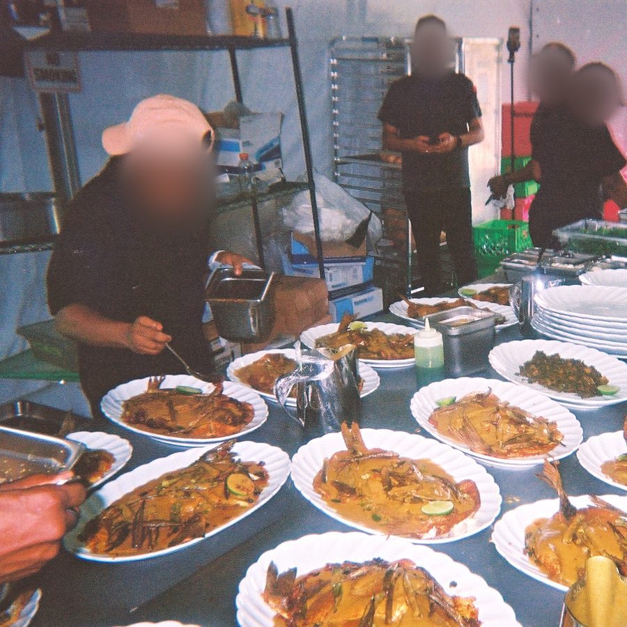Whole fried fish being plated in a busy event kitchen