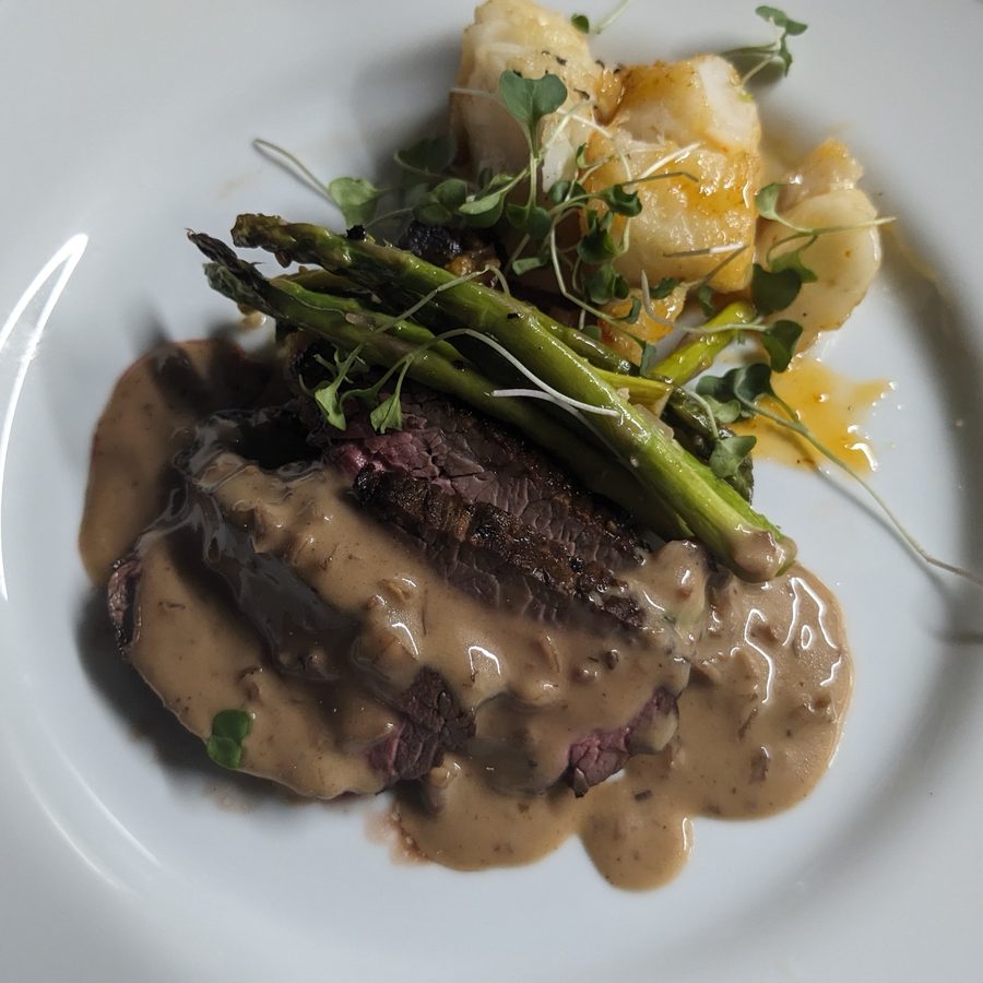 Seared steak in cream pan sauce with asparagus, scallops and microgreens